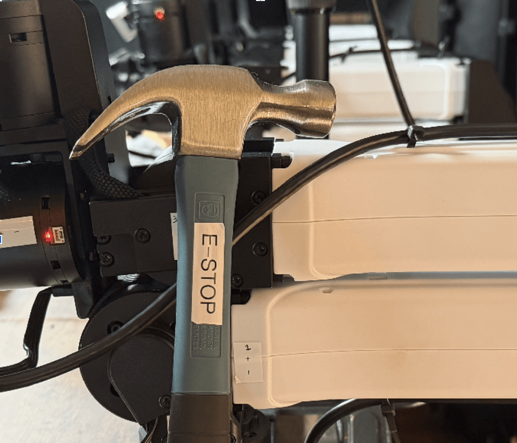 A hammer labelled e-stop reseting against a robotic arm.