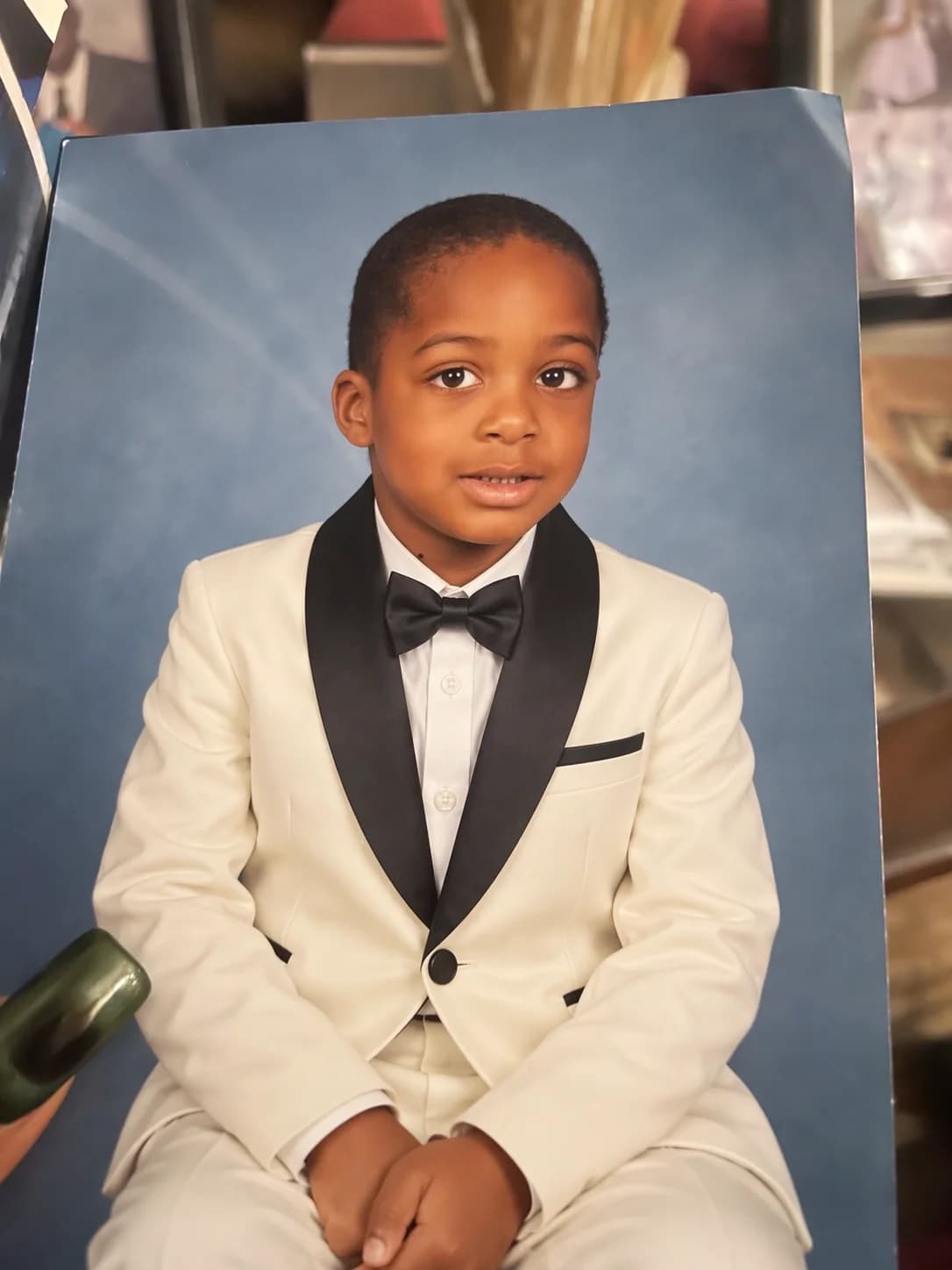 The edited printed portrait shows the child in an ivory tuxedo with black lapels and a black bow tie, preserving the pose and blue background.