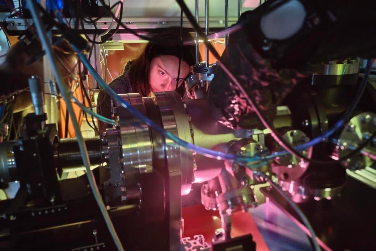 A person working on an extremely complex piece of scientific machinery with a pinkish light emanating from one portion of its gleaming components.